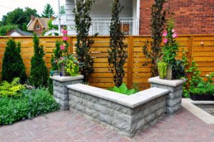 Vertical fence with landscaped shrubbery, featuring paver patio and stone bench