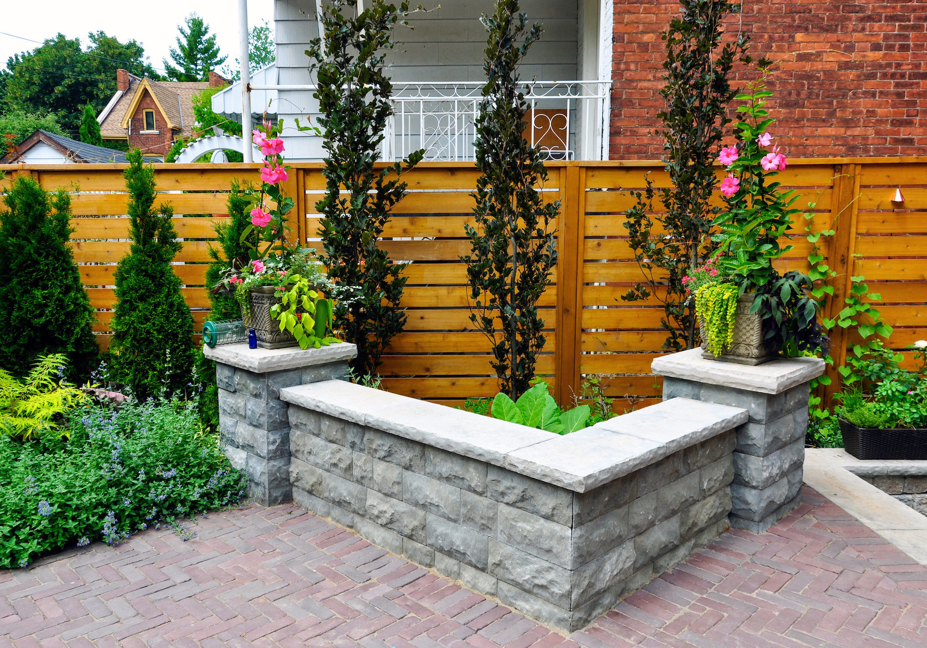 A retaining wall with natural stone coping and pillars added additional seating for entertaining in a small urban backyard garden